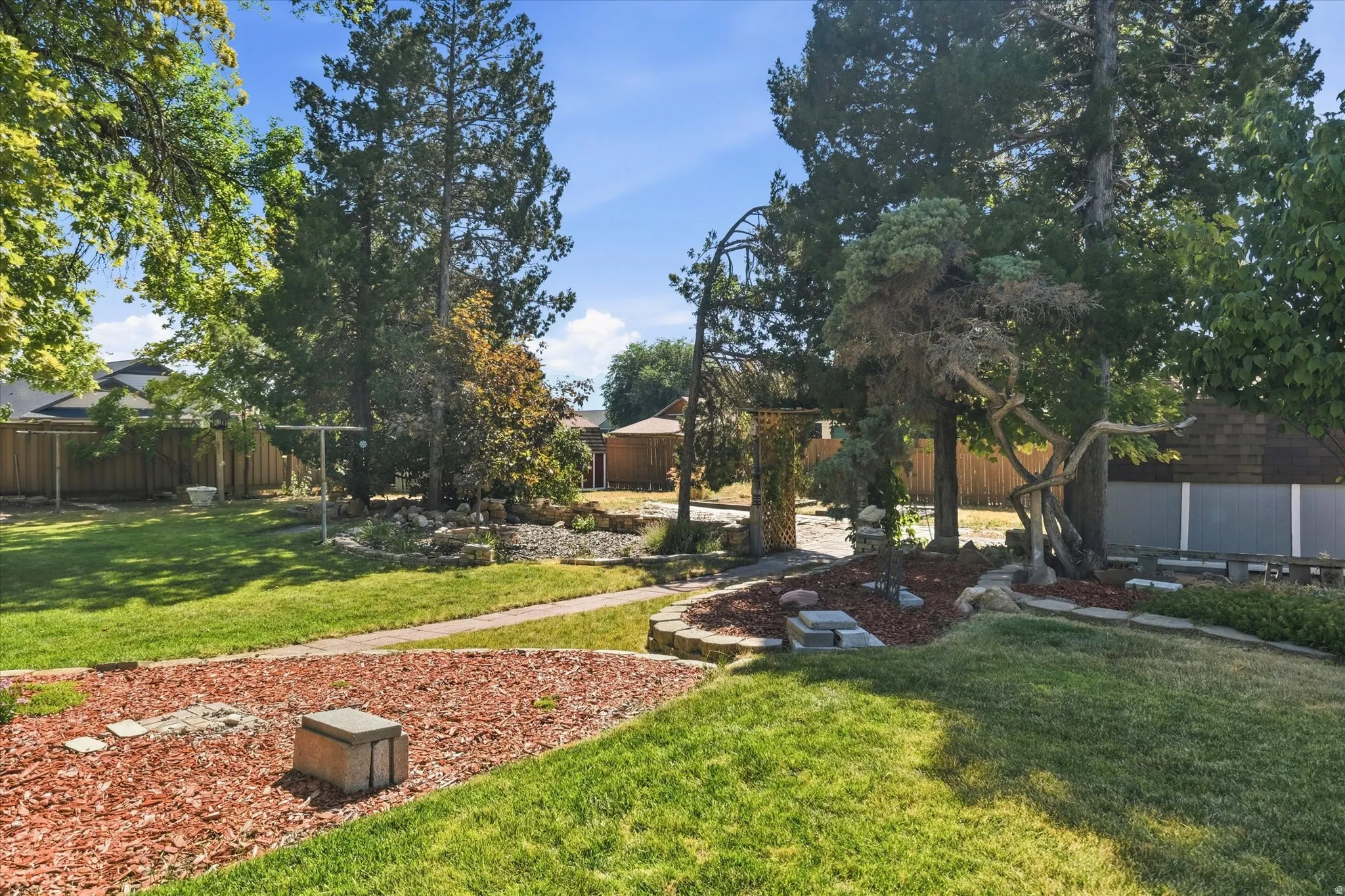 Expansive backyard featuring mature trees, landscaped rock features, and a stone pathway
