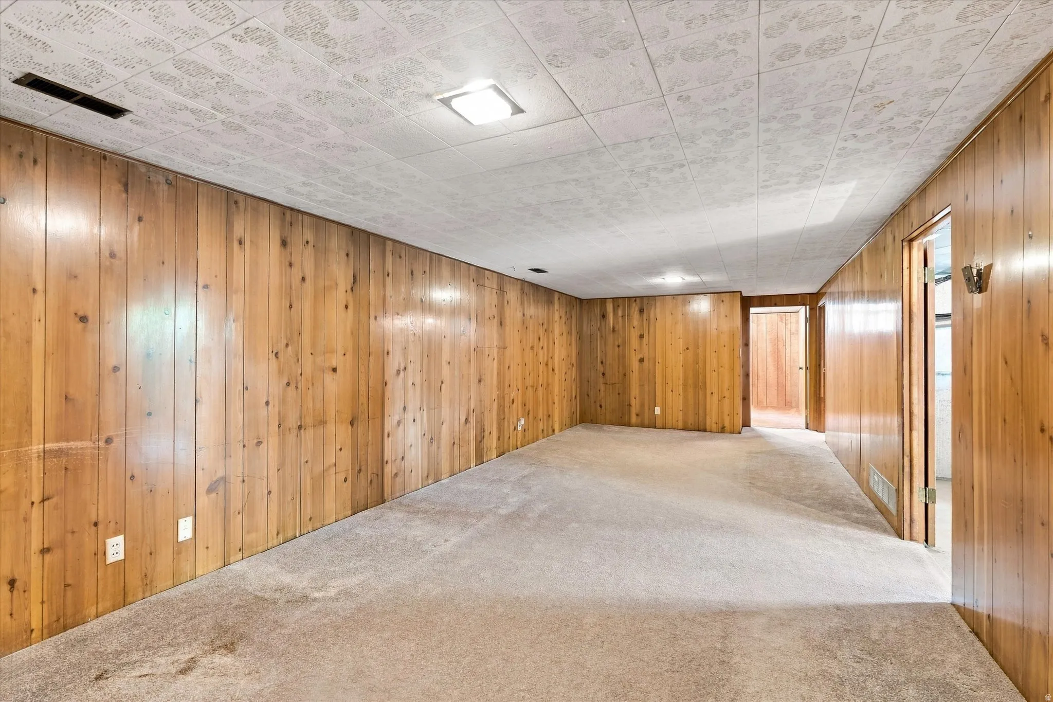 Expansive room featuring wood paneling throughout, light-toned carpet flooring, and a patterned ceiling with flush-mount lighting fixtures