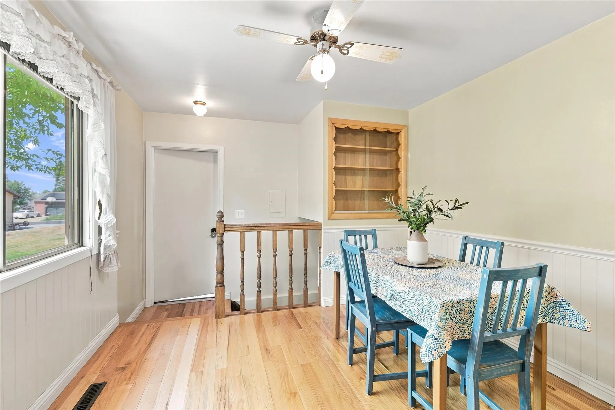 Dining area featuring wood-finish flooring, wainscoting, a built-in display shelf, and a ceiling fan with integrated lighting