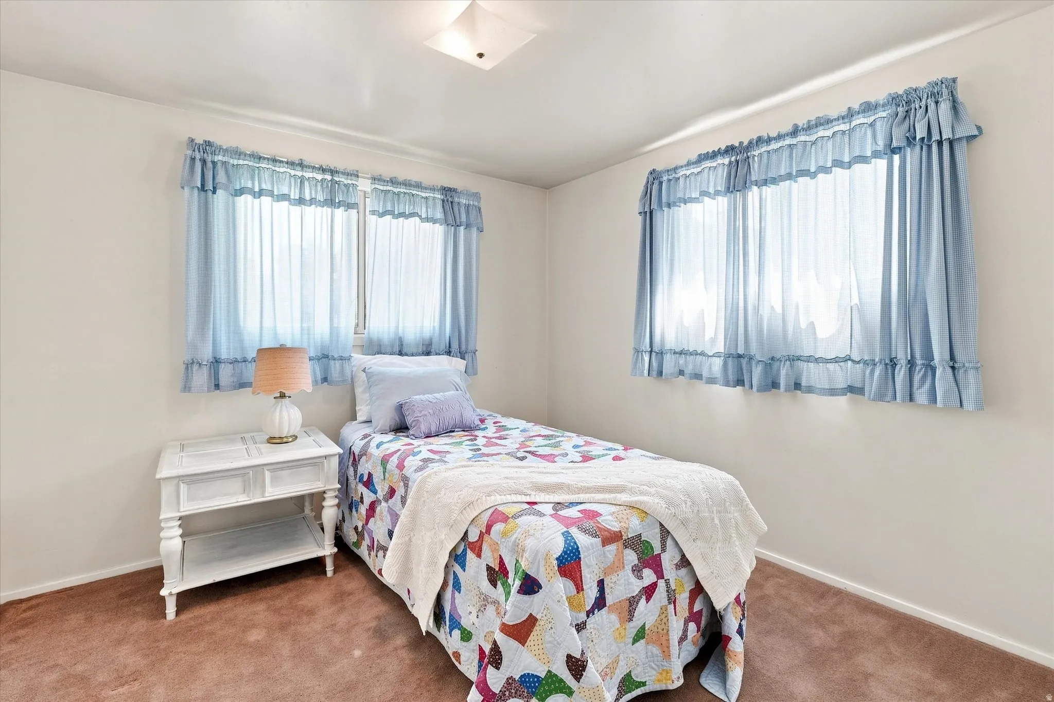 Light-filled room featuring two windows with valances and sheers, neutral wall paint, and brown carpeting
