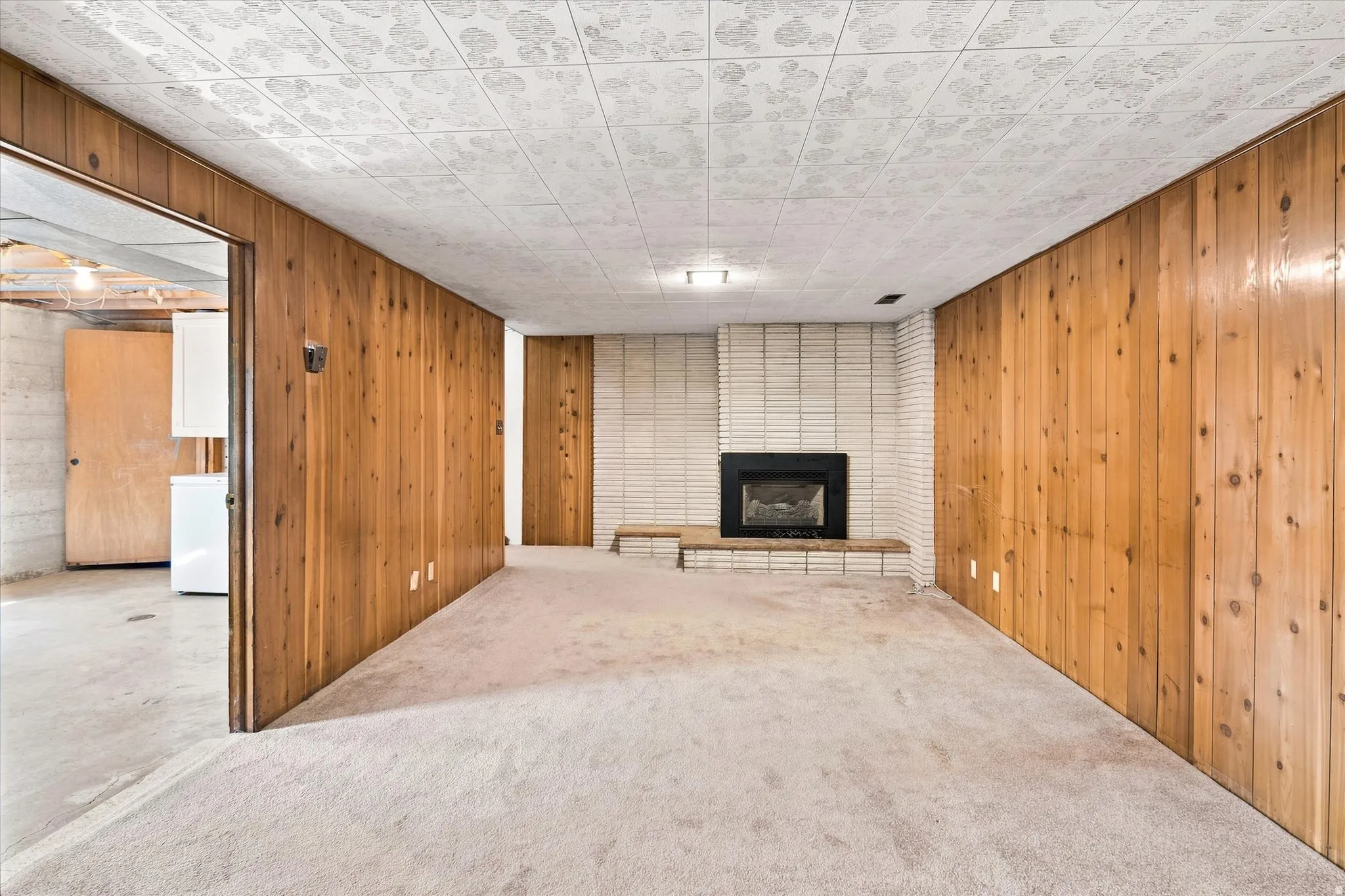 Room featuring wood-paneled walls, carpet flooring, and a fireplace with a white brick surround