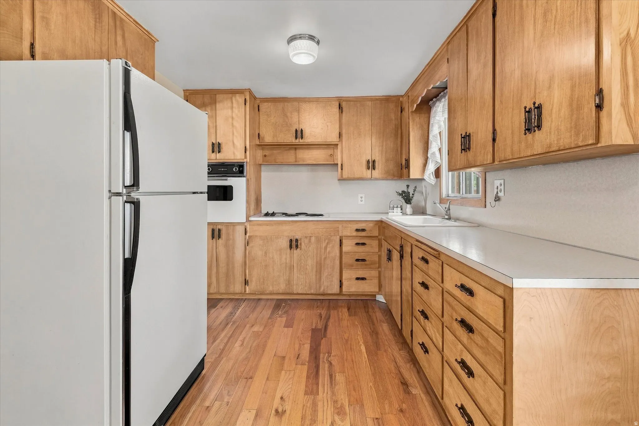 Kitchen featuring wood-finish flooring, light wood cabinetry with dark hardware, white countertops, built-in wall oven, and a gas cooktop