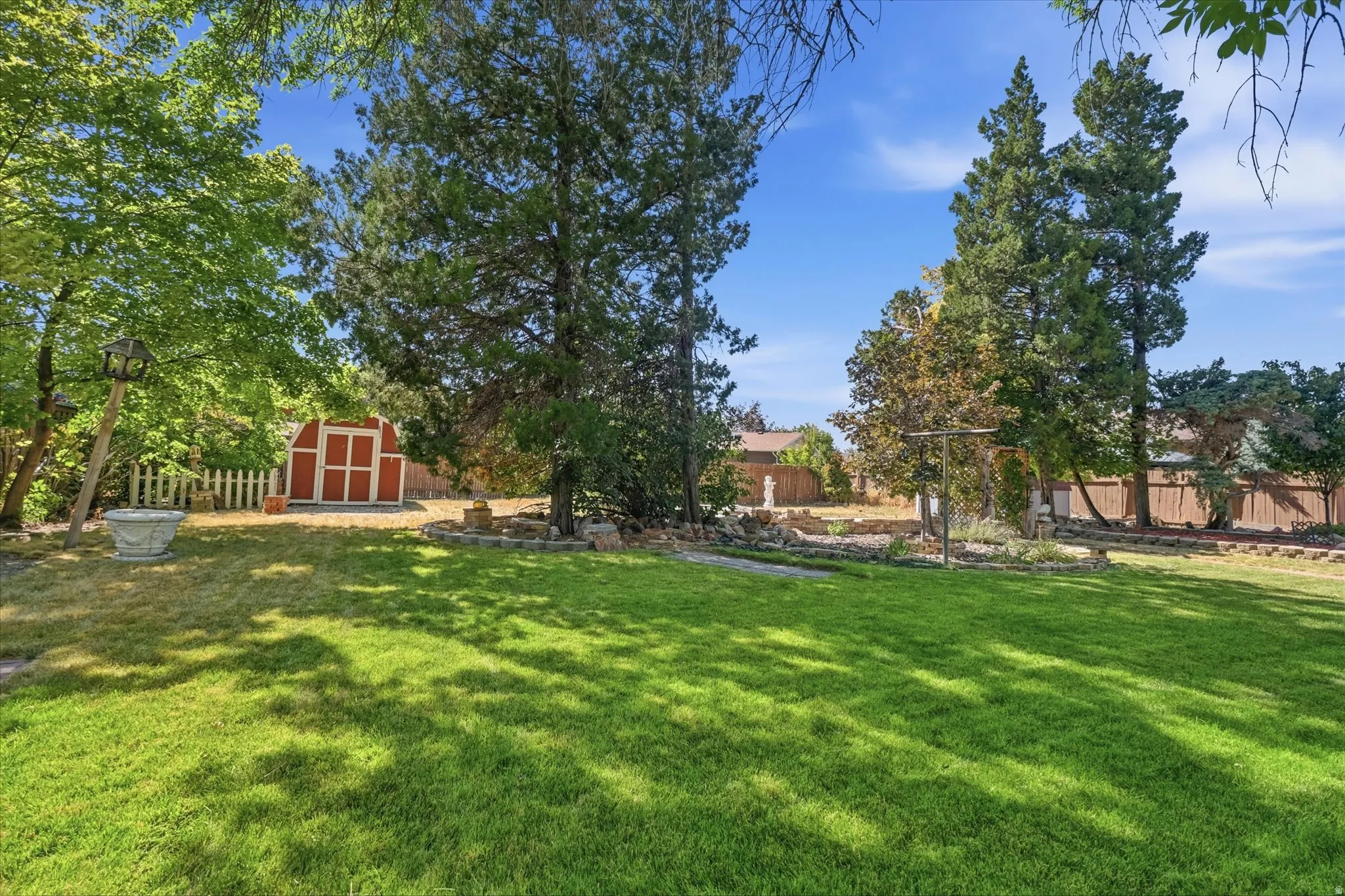 Expansive green lawn with mature trees and a red and white detached storage shed