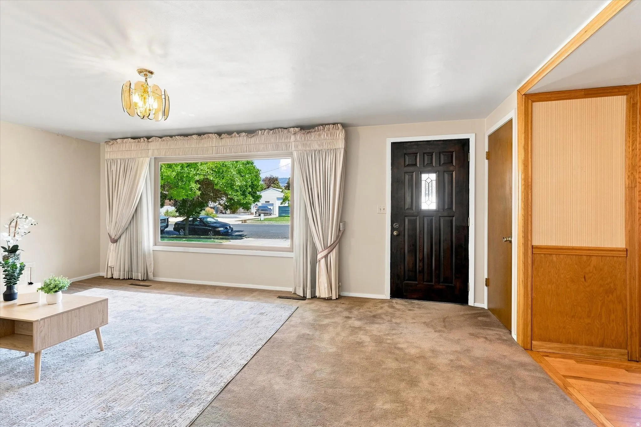 Bright and spacious foyer featuring hardwood-finish flooring, neutral wall tones, and abundant natural light from a large front-facing window with custom drapery