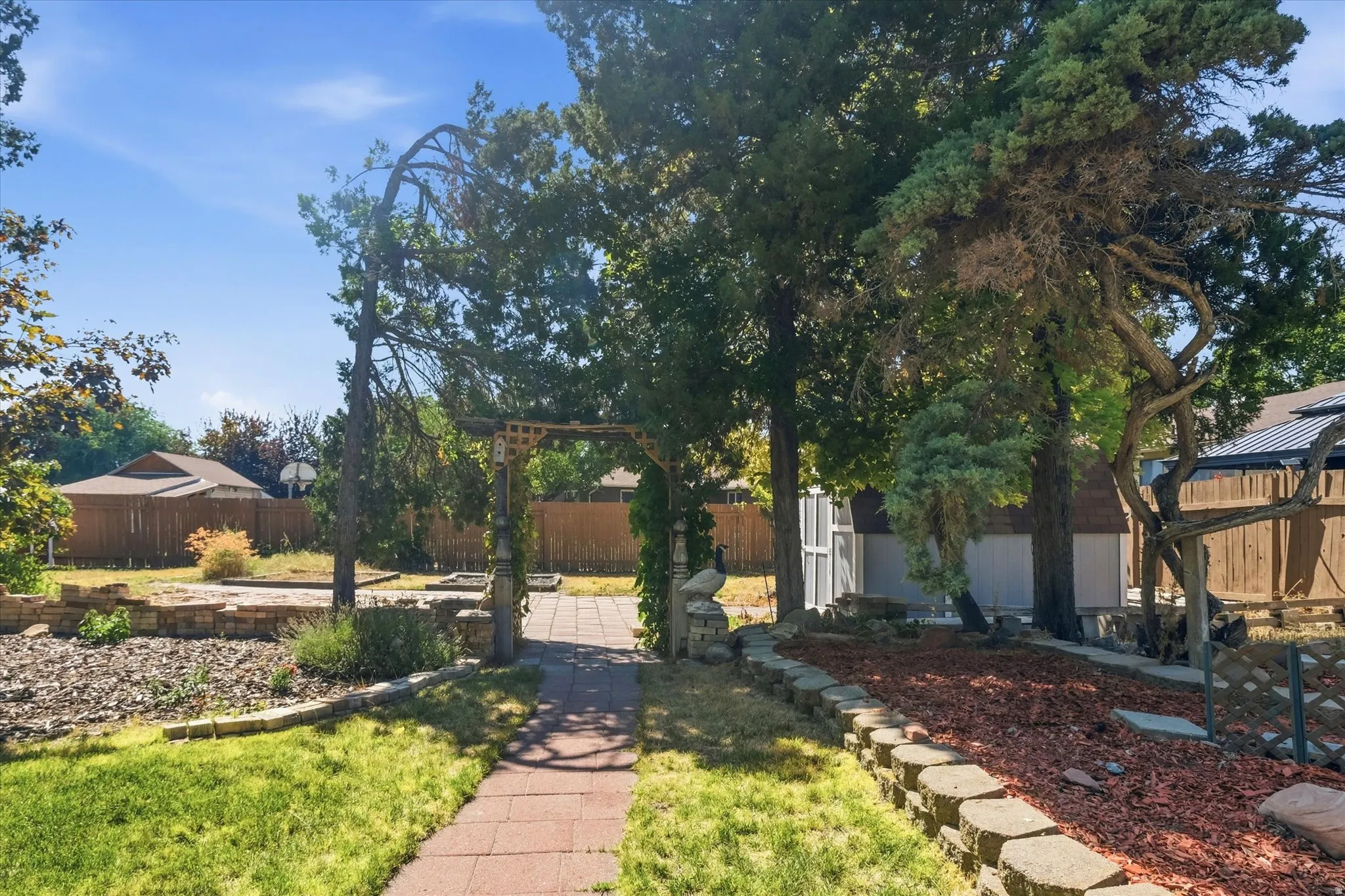Landscaped backyard featuring a paver pathway and a wooden trellis entrance