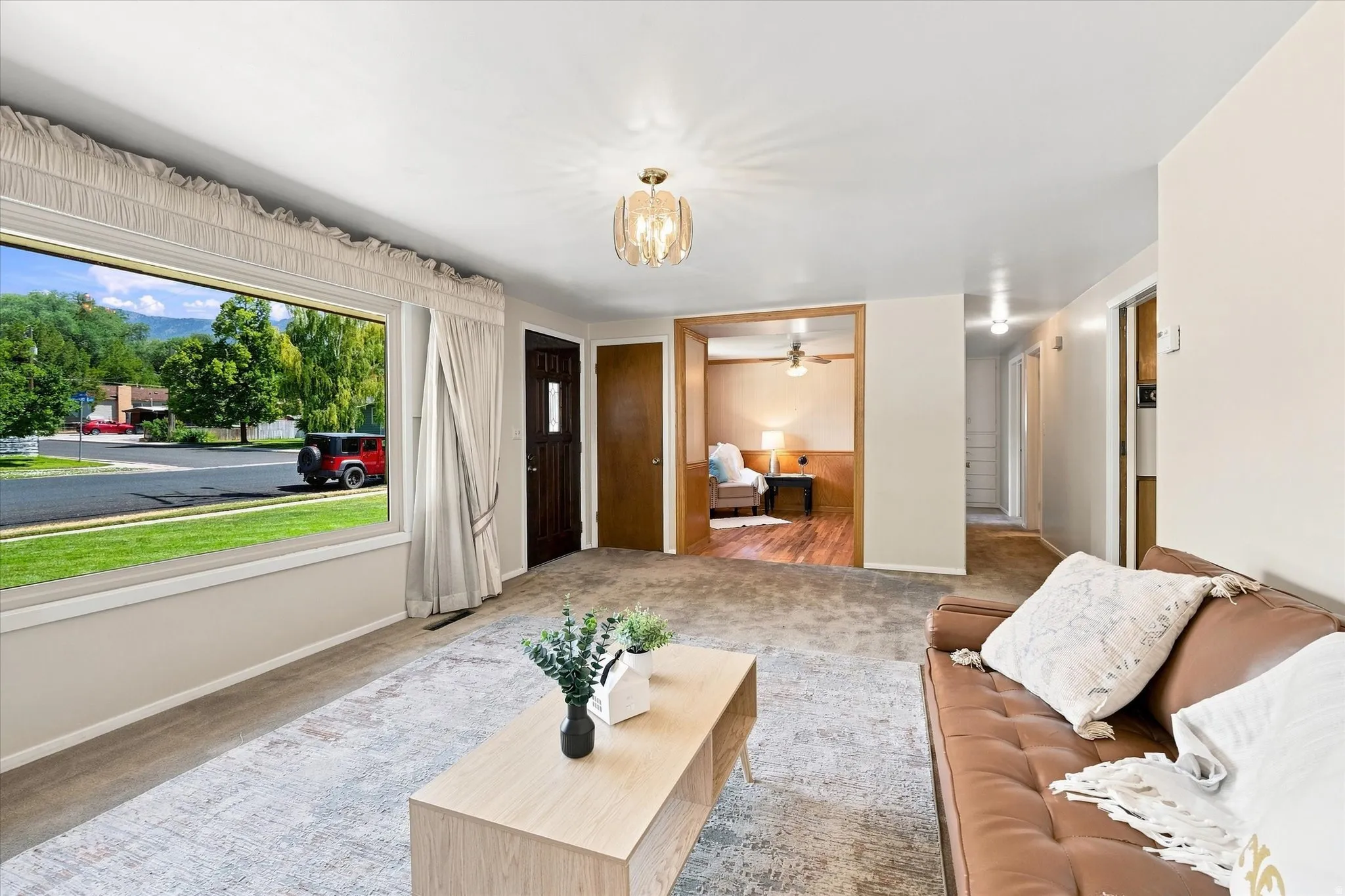 Expansive living area featuring a large picture window, overhead decorative light fixture, and wood-finish flooring