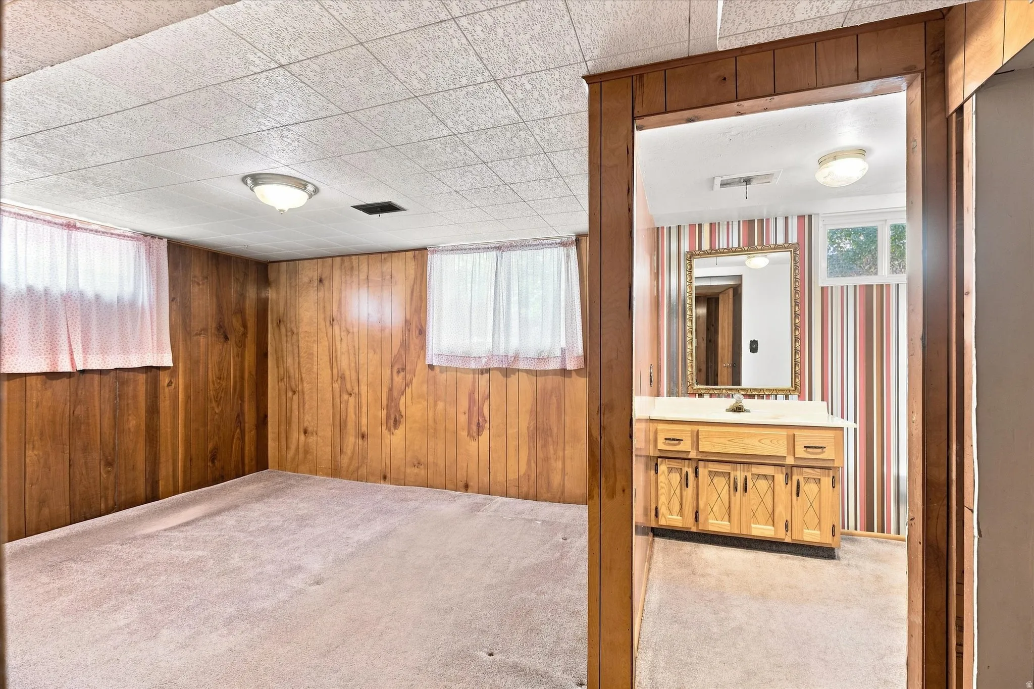 Versatile room featuring wood paneling, two windows, and textured ceiling tiles