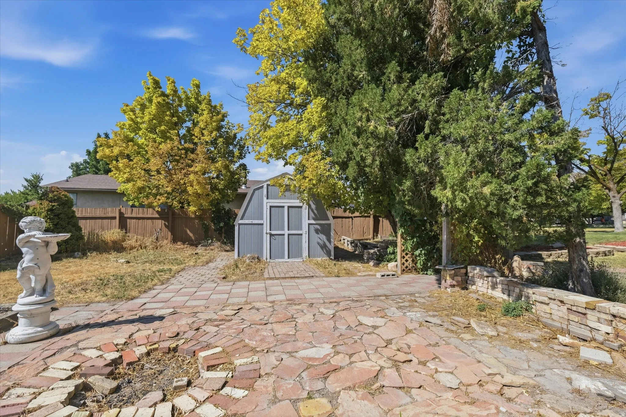 Outdoor patio area featuring a stone and brick paver surface, a stone retaining wall, and mature trees