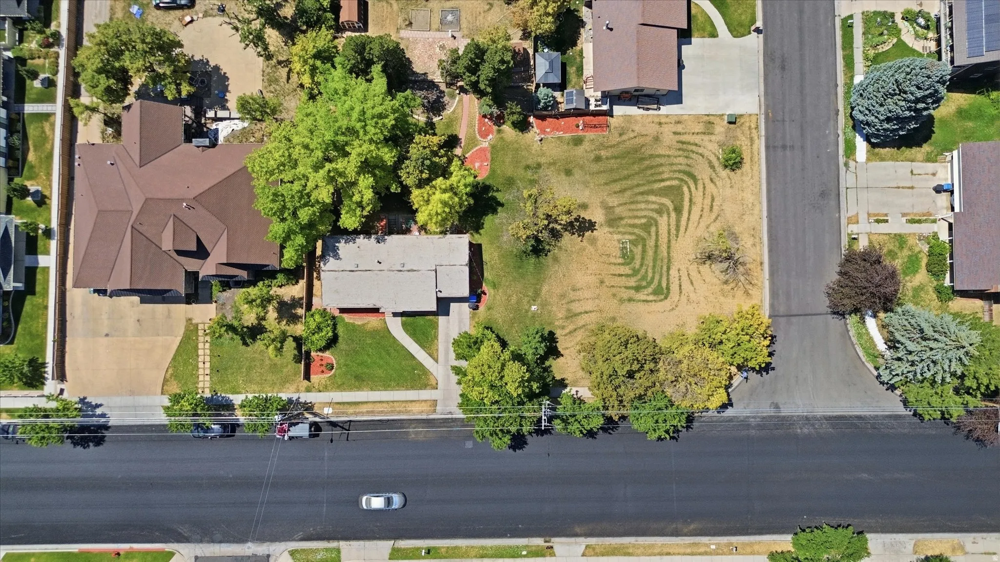 Aerial property view featuring a main residence with a brown shingle roof, an adjacent building with a lighter-colored roof, and a large lawn area with visible landscaping patterns