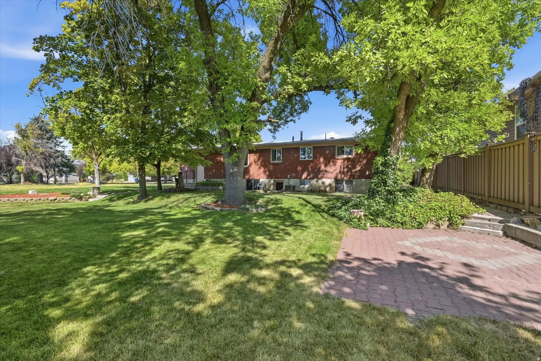 Expansive backyard featuring a manicured lawn, mature trees, and a brick paver patio