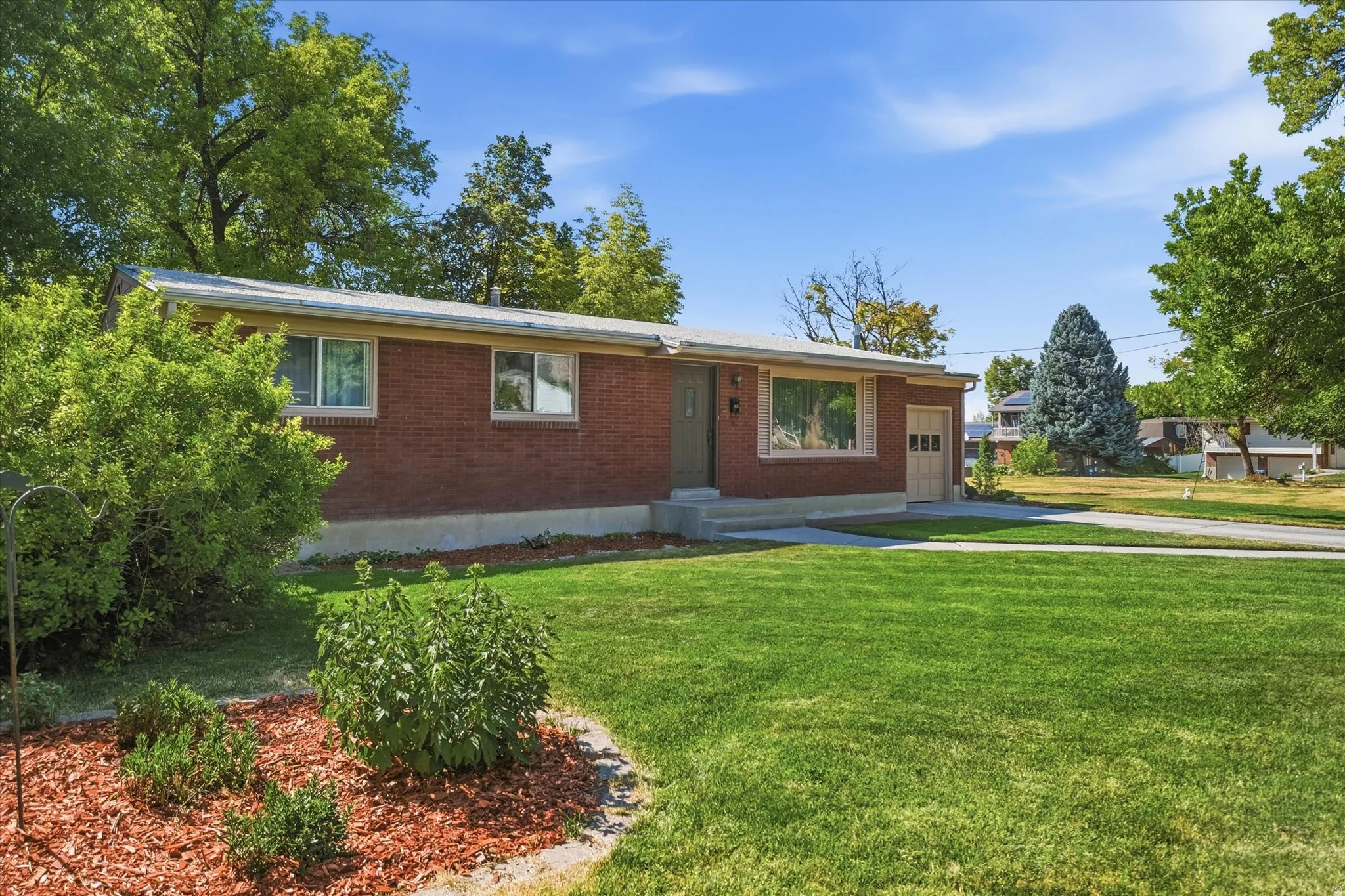 Brick-faced residence featuring a prominent front lawn and a concrete driveway leading to an attached garage