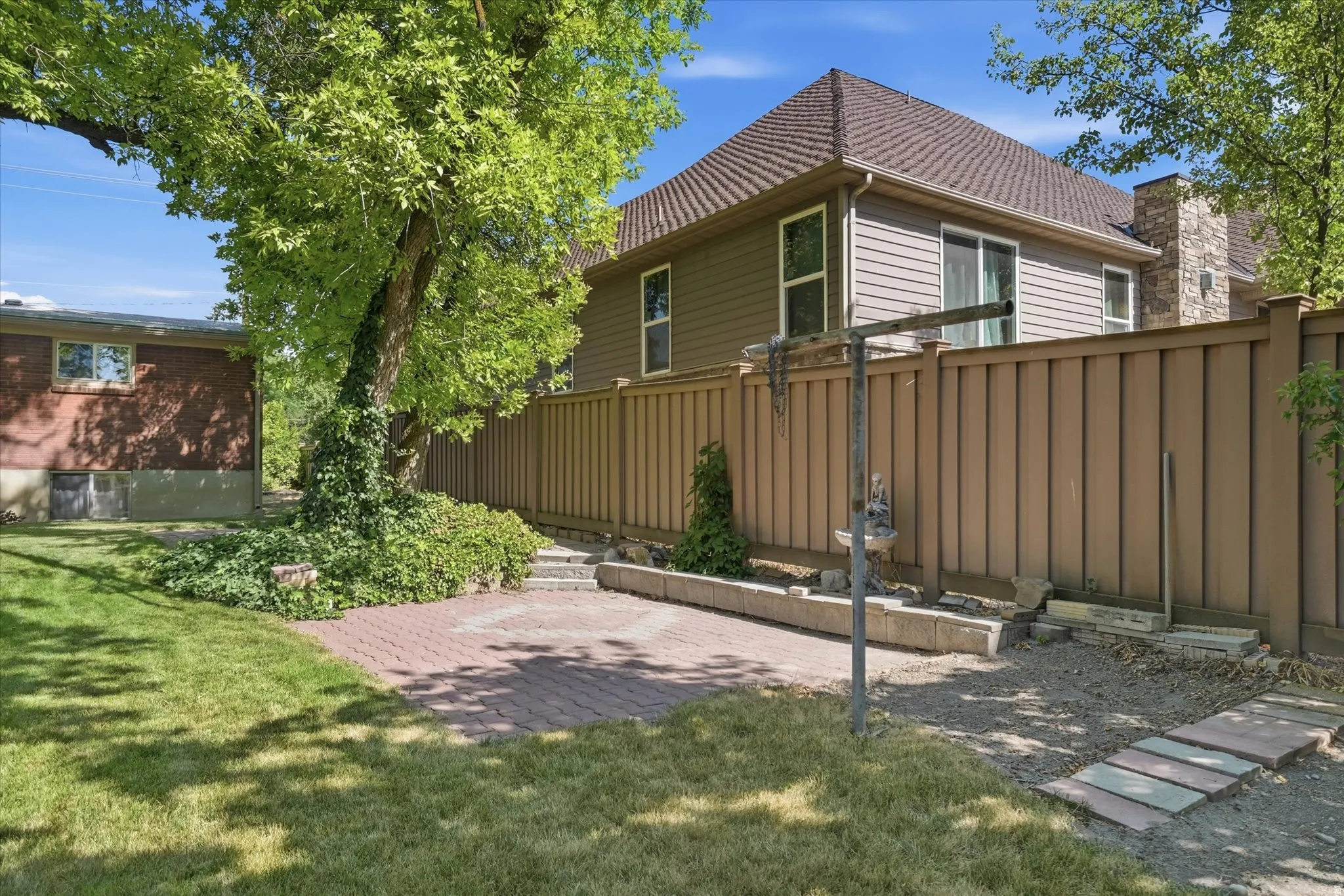 Expansive backyard featuring a brick paver patio, a manicured lawn, and mature trees