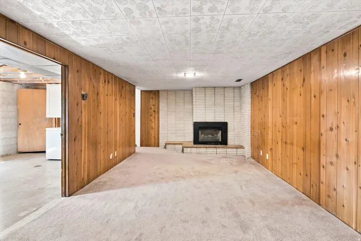 Room featuring wood-paneled walls, carpet flooring, and a fireplace with a white brick surround