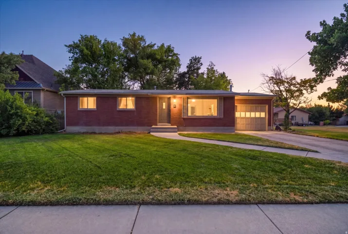 Brick exterior featuring a two-car garage with a panel door, concrete driveway, and front lawn