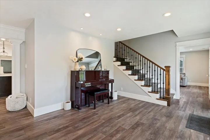 Welcoming foyer showcasing rich wood-finish flooring, recessed ceiling lighting, and a grand staircase with wooden handrails and metal balusters