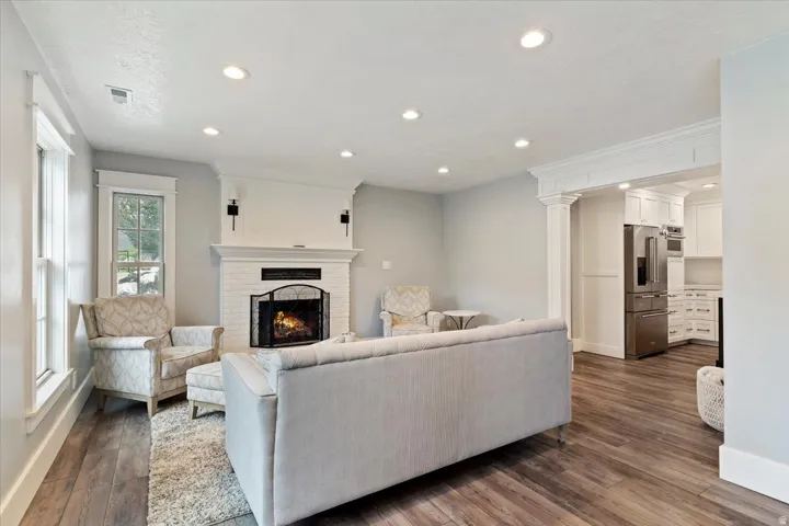 Elegant open-concept living space featuring a wood-finish plank floor, recessed ceiling lighting, and a gas fireplace with a white surround and black insert