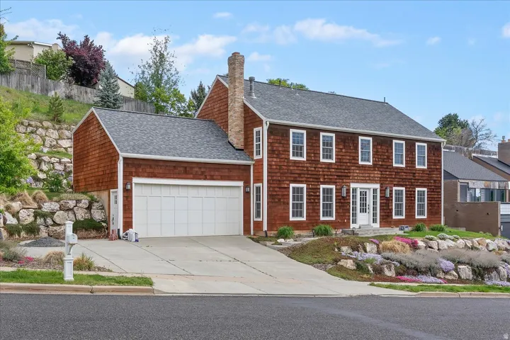 Charming Colonial-style residence featuring a brick exterior with white-trimmed windows, a two-car garage with white paneled doors, and a slate-shingled roof