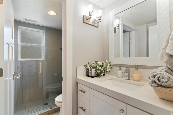 Spa-inspired primary bathroom featuring a frameless glass-enclosed shower with tile surround, dual vanity with white quartz countertop, chrome fixtures, recessed ceiling lighting, and large mirror with sconce lighting