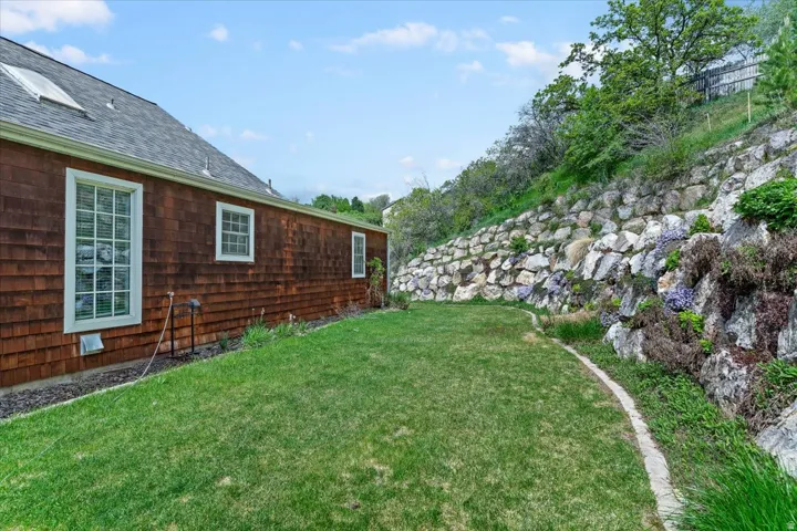 Expansive side yard featuring a manicured lawn, natural rock retaining wall, and mature landscaping