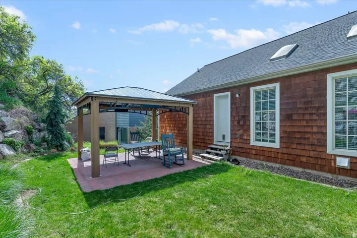 Charming cedar-shake exterior with expansive rear grounds featuring a manicured lawn, mature landscaping, and a covered patio structure with integrated seating area