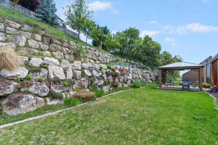 Expansive grounds featuring a manicured lawn, mature landscaping, and a substantial stone retaining wall with natural strata detailing