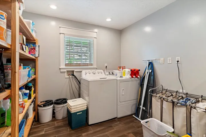 Dedicated laundry room featuring side-by-side washer and dryer with ample counter space, wood-finish flooring, generous storage cabinetry, and natural light from a shuttered window