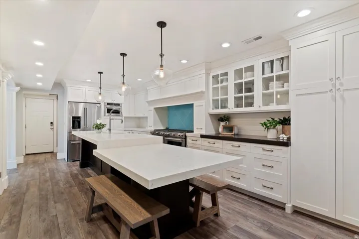 Spacious kitchen featuring two large islands with white countertops, white shaker cabinetry, stainless steel appliances, and wood-finish flooring
