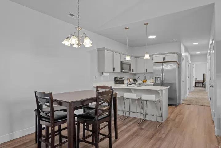 Open-concept kitchen and dining area featuring stainless steel appliances, white cabinetry with hardware accents, a kitchen island with seating, pendant lighting, and wood-finish flooring throughout