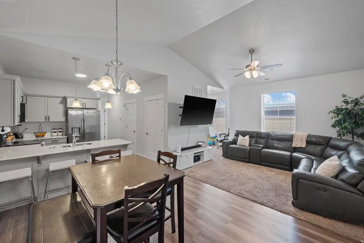 Open-concept living area featuring vaulted ceilings, wood-finish flooring, a contemporary kitchen with light-toned cabinetry and stainless steel appliances, and a dining area with a chandelier