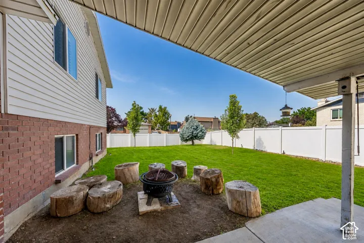 Expansive backyard featuring a manicured lawn, white privacy fencing, and a dedicated fire pit area with tree stump seating