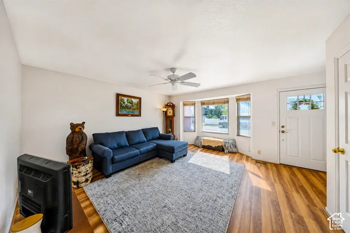 Bright living area featuring wood-finish flooring, a ceiling fan with light, and a prominent bay window