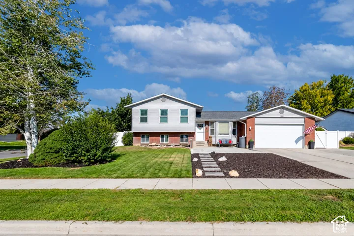 Split-level residence featuring a two-car garage, red brick accents, and a white fence
