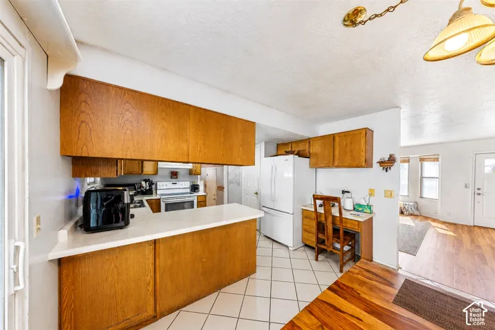 Kitchen featuring wood cabinetry, white tile flooring, white appliances, and a built-in desk area