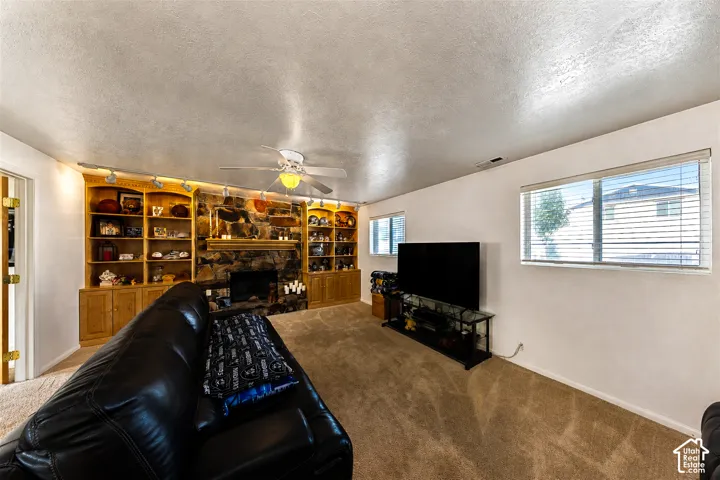 Living area featuring a stone-surround fireplace, built-in shelving, track lighting, and a ceiling fan with integrated lighting