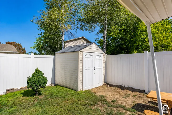 Fenced backyard with mature landscaping, storage shed featuring white finish and peaked roof design, and covered patio structure