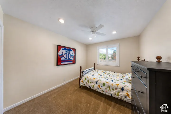 Carpeted room featuring a ceiling fan, recessed lighting, and a window with white louvered shutters