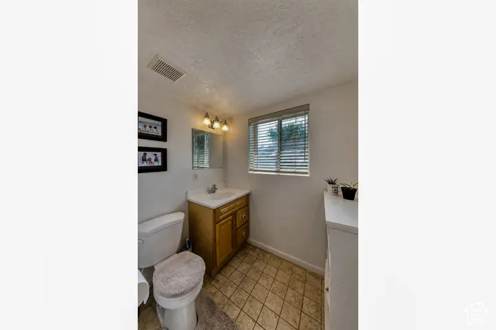 Functional bathroom featuring a wood-finish vanity with integrated sink, tile flooring, and natural light from a window with plantation shutters