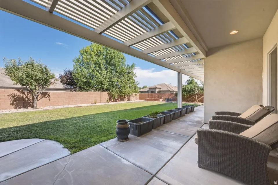 Expansive covered patio with motorized louvered pergola offering customizable shade, paired with comfortable seating areas overlooking a manicured lawn and mature landscaping