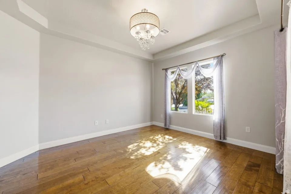Bright and spacious room featuring gleaming wood-finish flooring, recessed ceiling detail with integrated lighting fixture, and dual glass doors with transom windows framing natural light