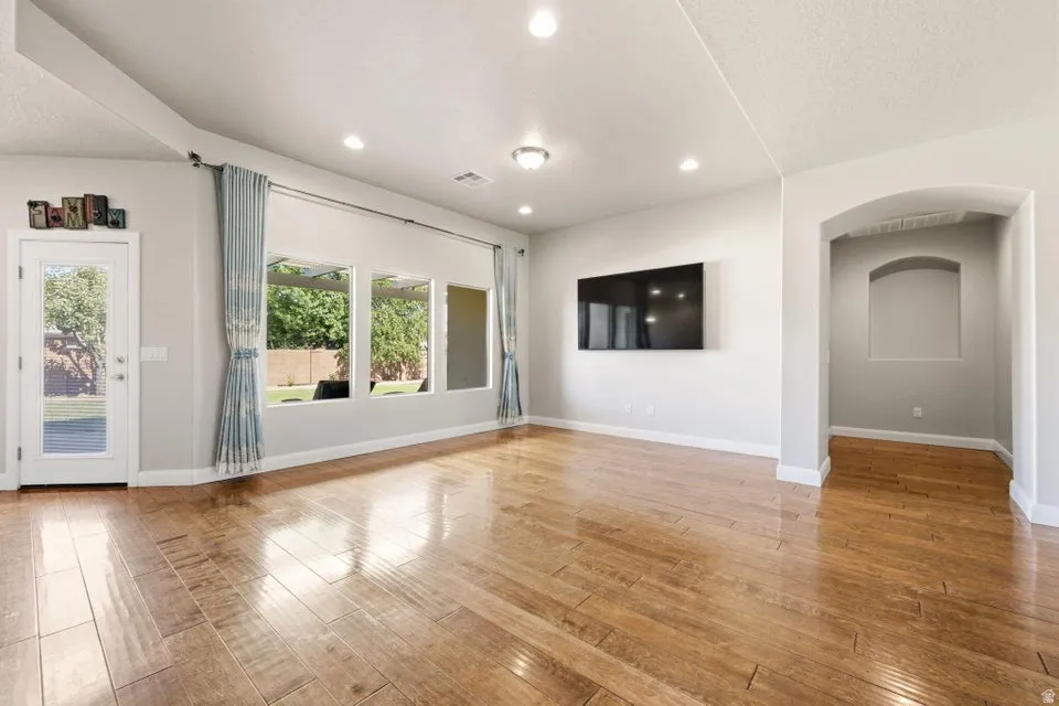 Spacious open-concept living area featuring pristine wood-finish flooring throughout, recessed ceiling lighting, and abundant natural light from multiple glass doors and windows