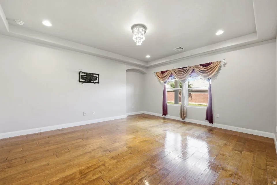 Spacious formal living room showcasing gleaming hardwood flooring, recessed ceiling with decorative chandelier, and tall windows dressed with elegant drapery