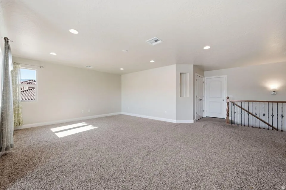 Spacious upper-level bonus room featuring neutral carpet flooring, recessed ceiling lighting, and abundant natural light from a large window