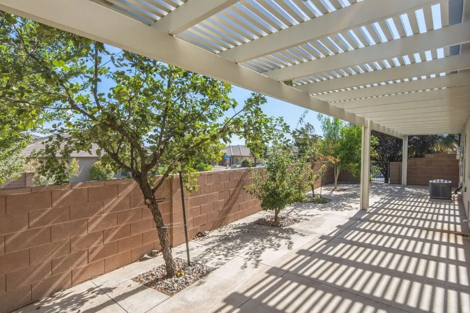 Expansive patio featuring a white slatted pergola, concrete flooring, and a privacy wall