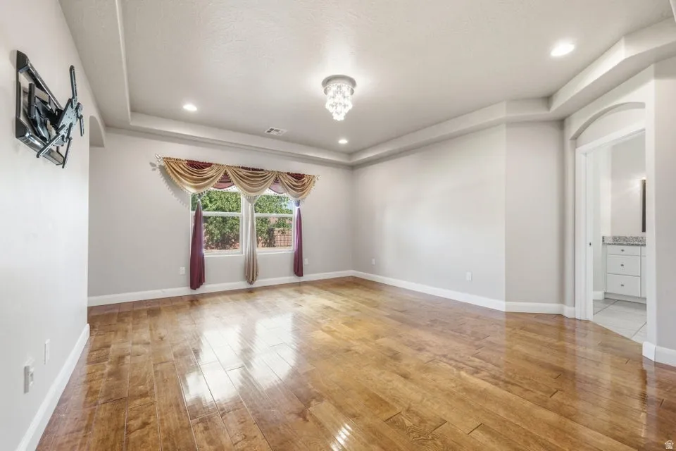 Spacious room featuring wood-finish flooring and a tray ceiling with recessed lighting