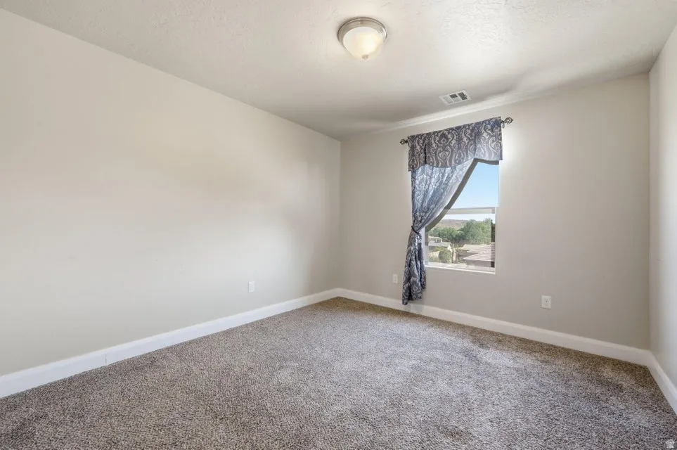 Spacious bedroom featuring neutral carpeting, fresh paint, and abundant natural light from the window