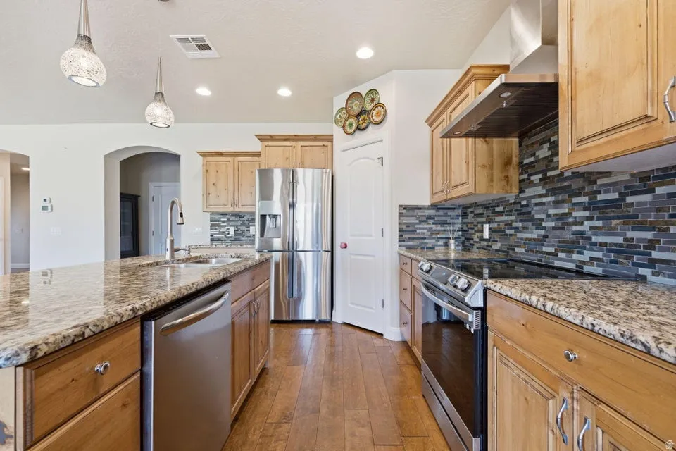 Galley-style kitchen showcasing warm wood cabinetry, granite countertops, stainless steel appliances, and a mosaic tile backsplash