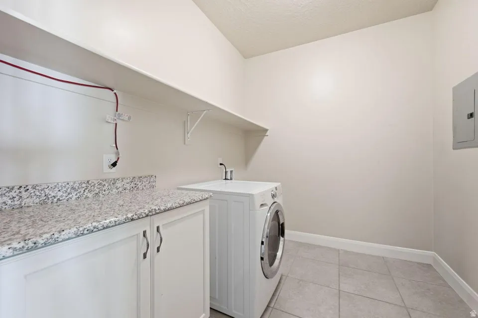 Dedicated laundry room featuring white cabinetry with brushed nickel hardware, speckled granite countertop, front-load washer, pedestal sink with chrome faucet, tile flooring, and abundant natural light from transom window