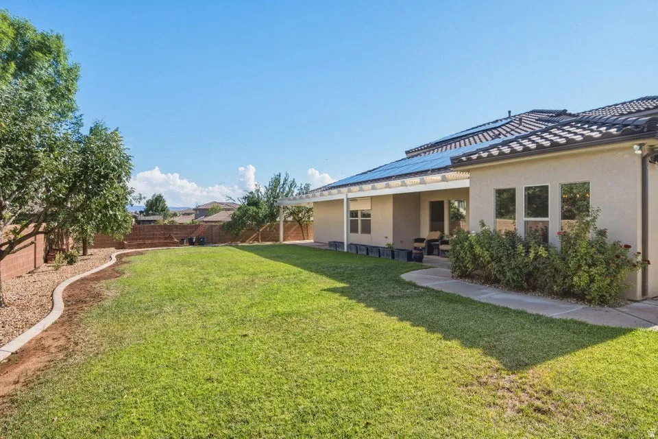 Expansive backyard featuring a lush lawn, mature trees, concrete patio, and stucco exterior with multiple windows