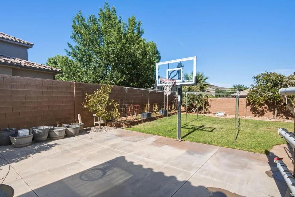 Expansive backyard featuring a concrete patio, a basketball hoop, and a grass lawn, all enclosed by a block wall