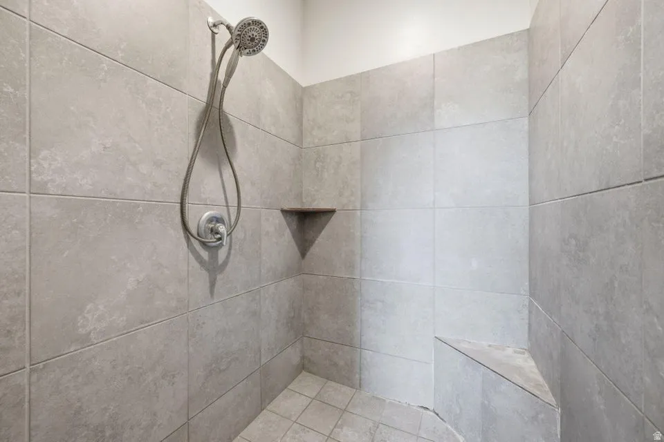 Tiled shower with a built-in seat, wall-mounted showerhead, and corner shelf